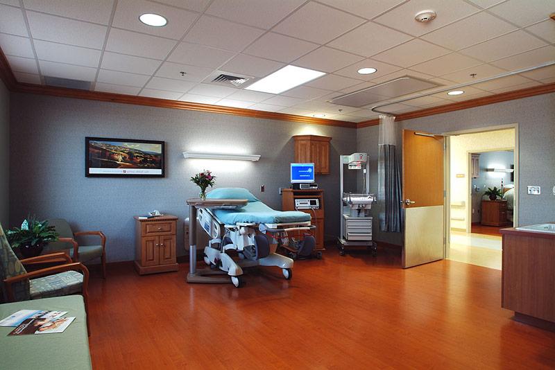 Interior photo of large hospital bedroom. Wood floors and cool grey walls.