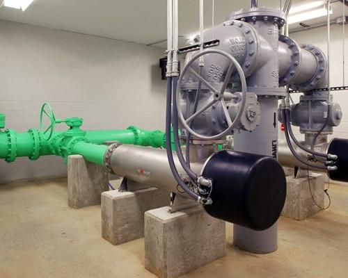 Large green and grey pipes with electrical and mechanical valves rest on concrete blocks inside the facility.